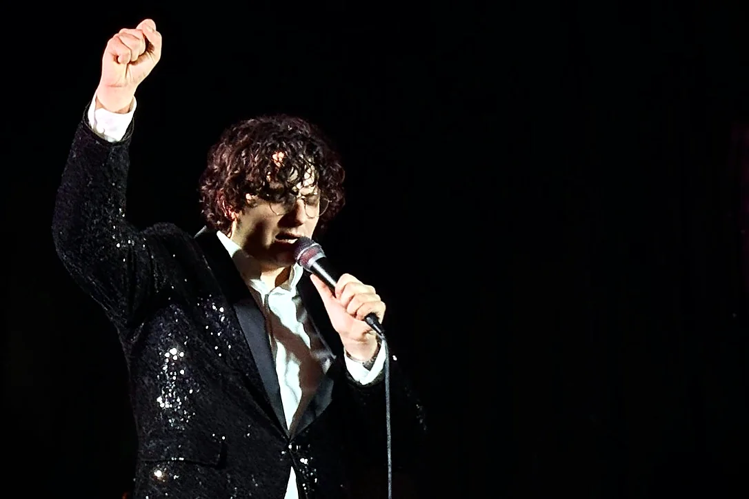 François Thiry en veste à paillettes, poing levé, chante dans le noir